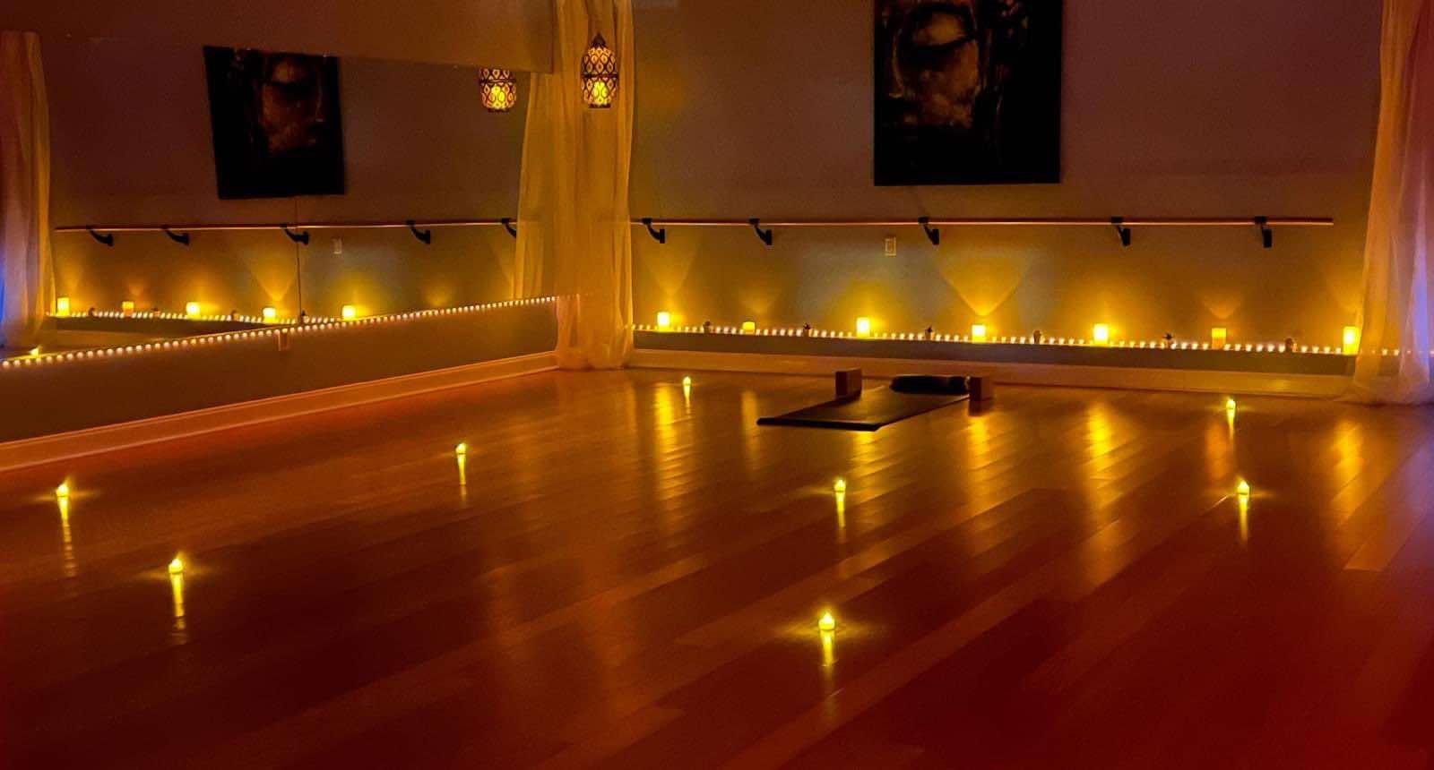 Yoga studio with dim lighting, candles, yoga mat, and props.
