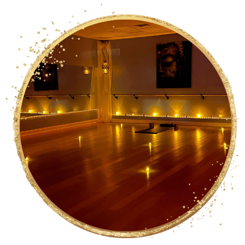 Dimly lit yoga studio with candles and wooden floor, featuring yoga mats and art on the walls.